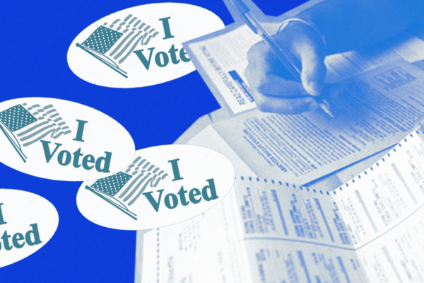 A blue-toned image of a person filling out a ballot. Their right forearm and hand are visible; they are holding a pen and filling out their ballot. "I Voted" stickers are overlaid on the left of the image.